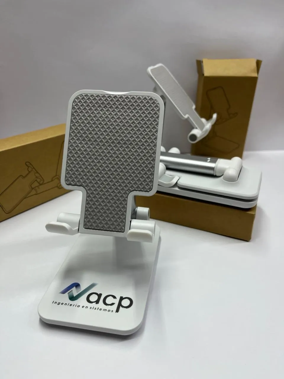 Soportes de celular blancos con el logo de ACP Ingeniería en Sistemas, junto a sus cajas